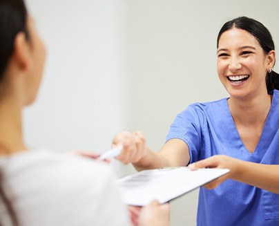 a woman in scrubs handing a patient forms on a clipboard