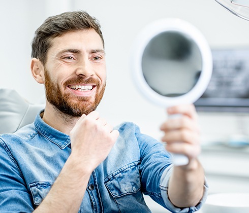 Man in dental office looking at smile in mirror