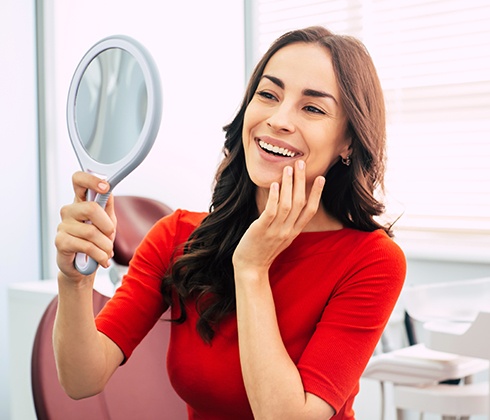 A young woman wearing a pink sweater and holding a clear aligner as part of her treatment with Invisalign in Midlothian