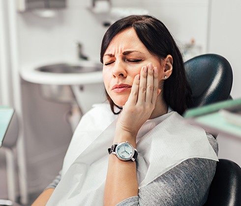 Woman at dental office for emergency dentistry holding cheek in pain