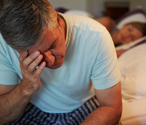 Frustrated man in need of sleep apnea therapy holding head