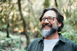 a smiling man with glasses hiking in a forest
